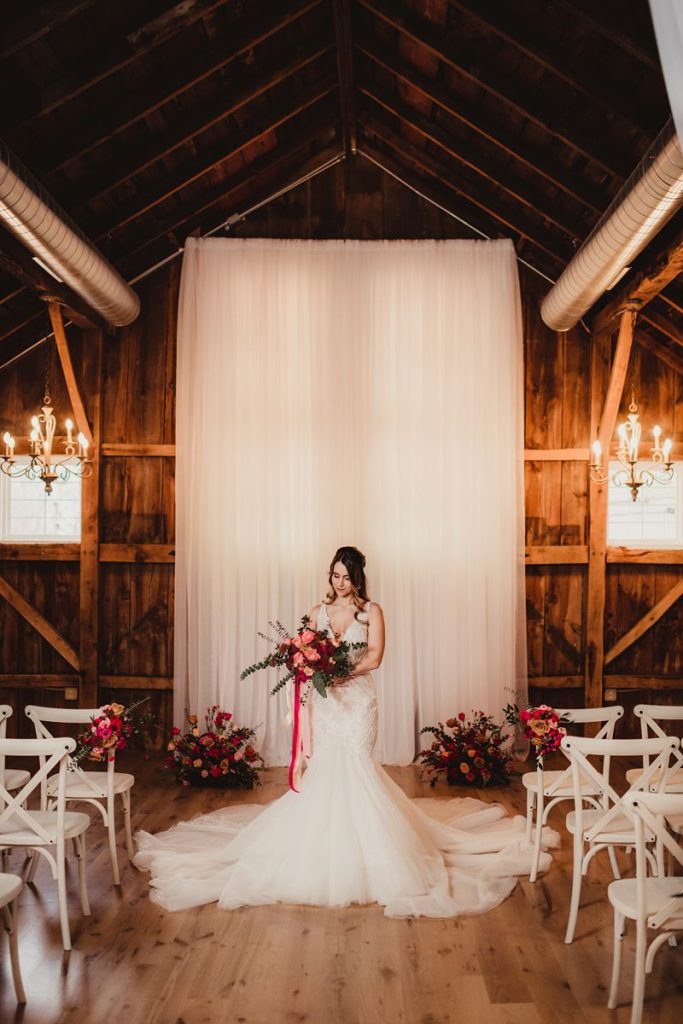 Bride holding bouquet at indoor ceremony space in barn.
